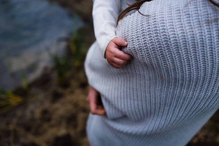 person in white jumper holding a baby,. the baby's hand holding onto jumper. they are standing outside